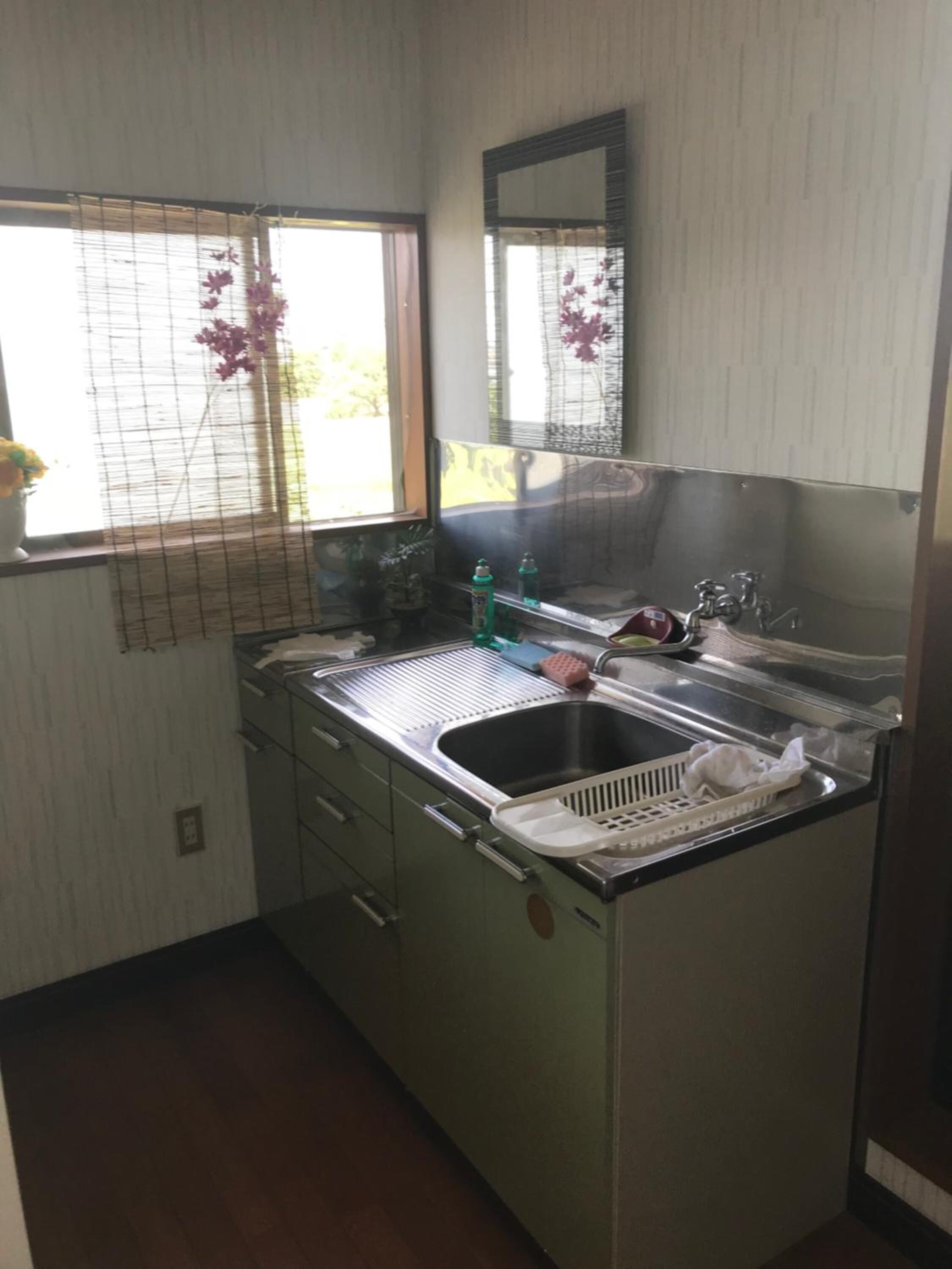 A compact kitchen with a sink, a mirror, and a window with a view of greenery outside.