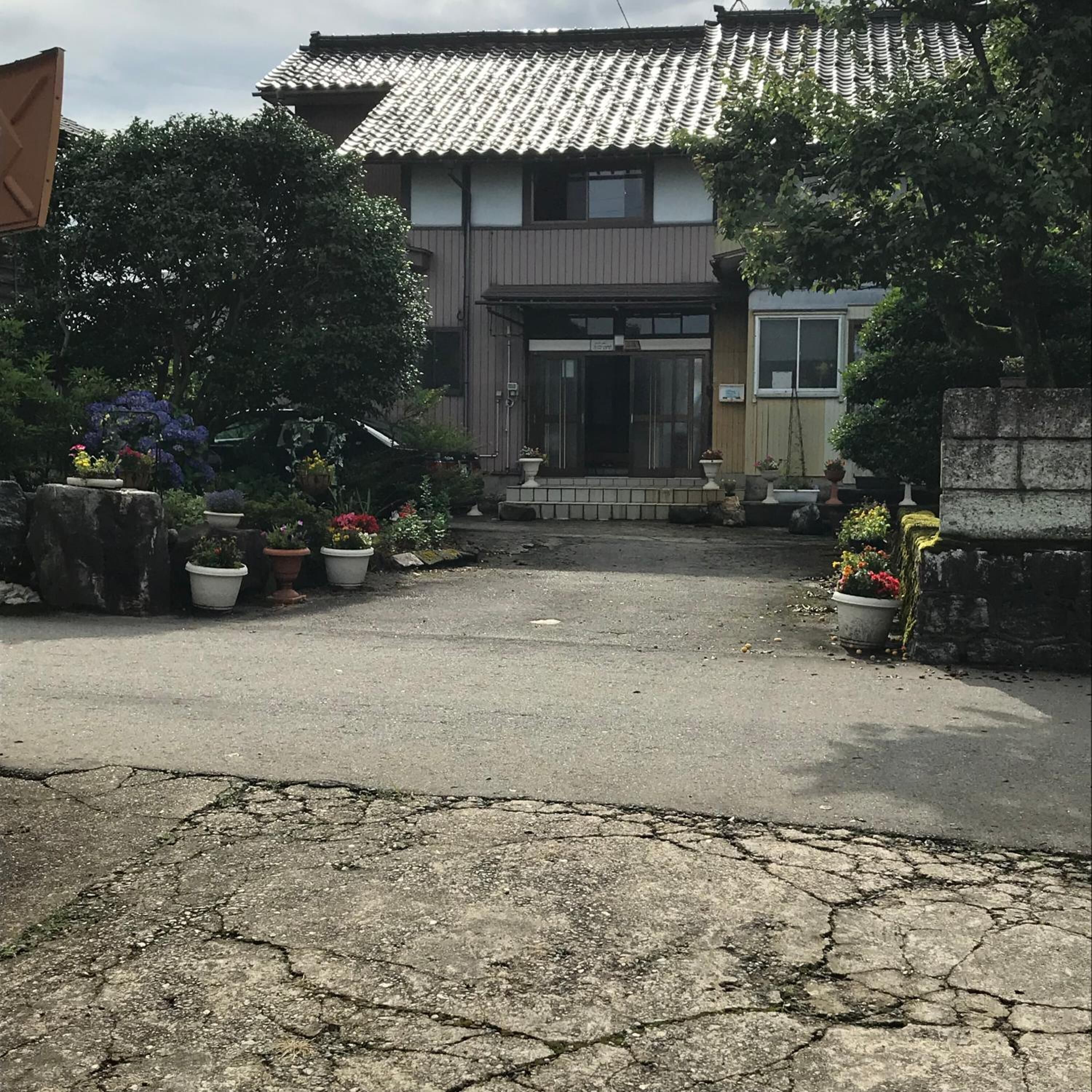 A traditional Japanese house with a tiled roof, a wooden entrance, and a garden with potted plants.