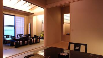 Una habitación tradicional japonesa con suelo de tatami, una mesa baja con un caja y puertas correderas que dan a un balcón con vistas al mar.
