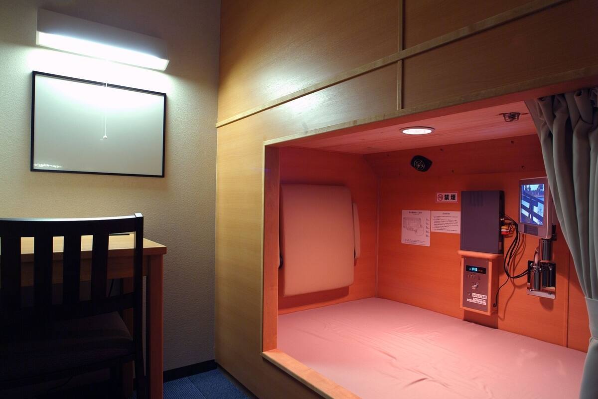 A small, single-bed room with a wooden headboard, a bedside table, and a wall-mounted TV.