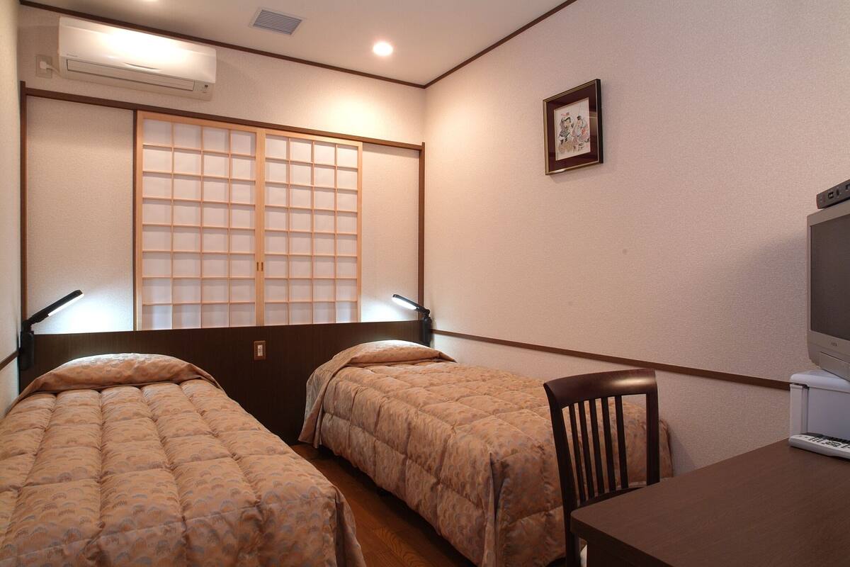A room with two beds, a desk with a computer, and a TV.