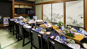 A traditional Japanese-style dining room with tatami flooring, a low table set with various dishes and utensils, and a view of a mountainous landscape through shoji screens. - Yoshikou (Takahama)