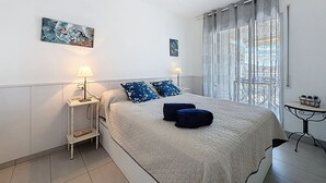 Une chambre à coucher avec un lit, deux tables de chevet avec des lampes, une fenêtre avec des rideaux et des œuvres d’art accrochées aux murs.