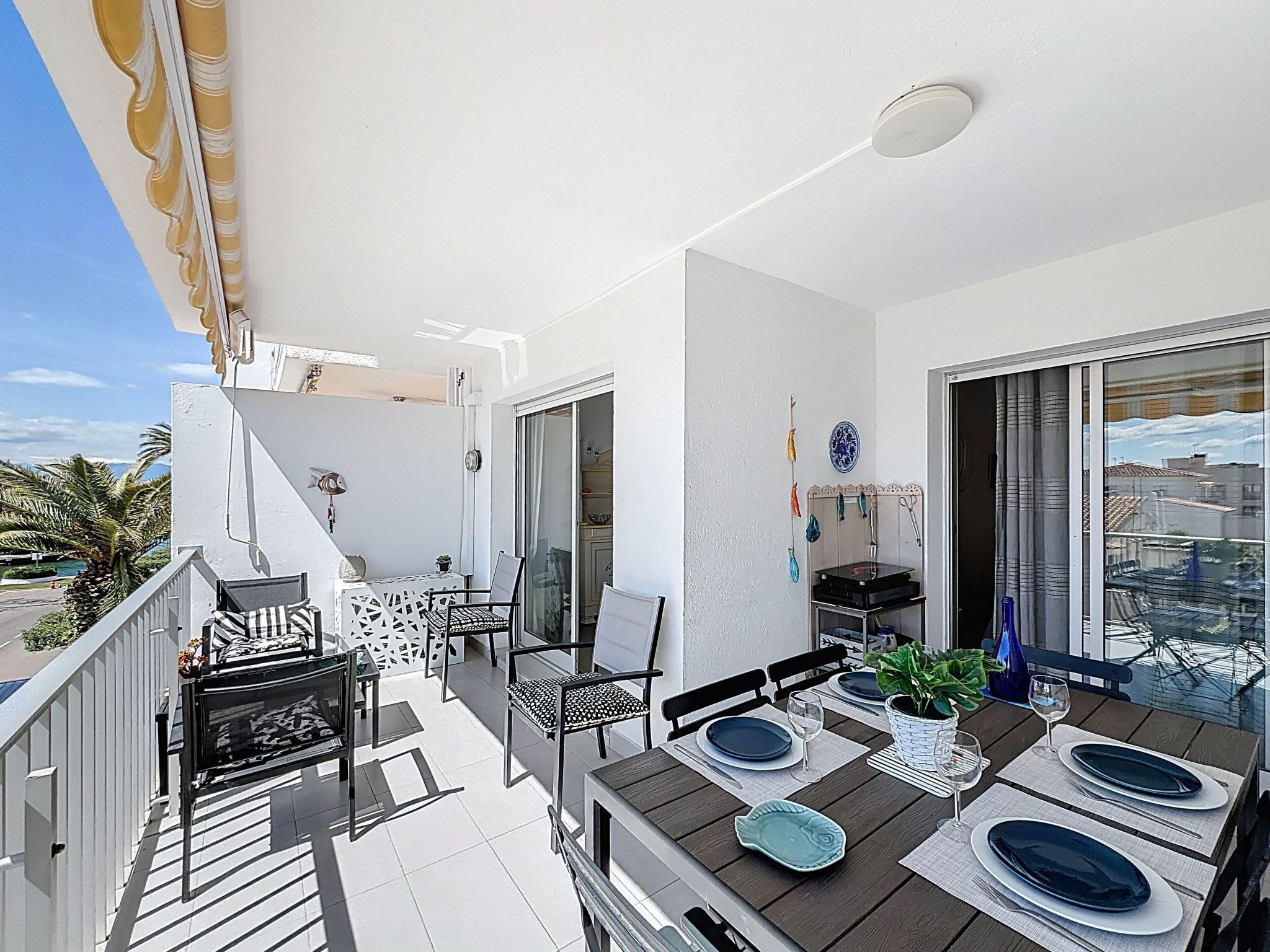 Un balcon avec une table à manger pour quatre personnes, des chaises, une petite table avec une chaise, et un escalier menant à un niveau supérieur.