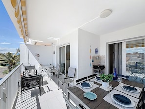 Ein Balkon mit Esstisch für vier Personen, Stühlen, einem kleinen Tisch mit Stuhl und einer Treppe, die zu einer erhöhten Ebene führt.