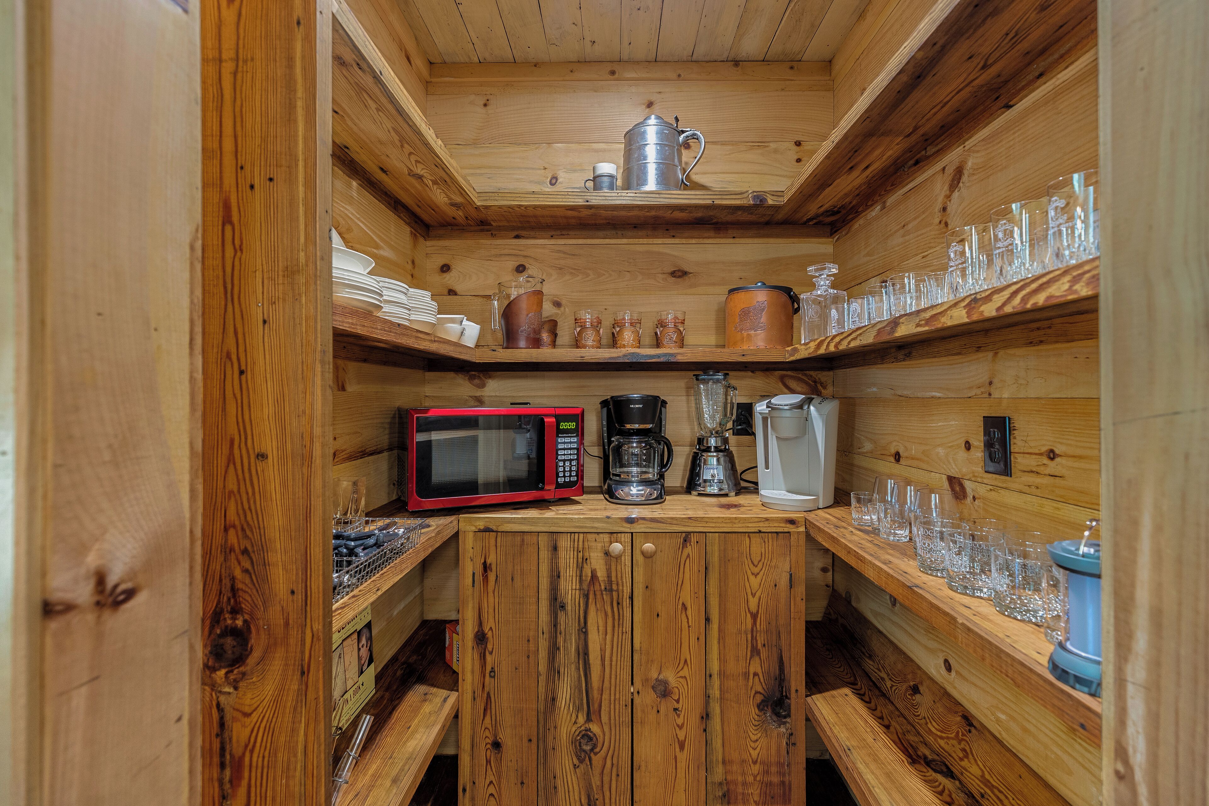 A compact kitchen with wooden cabinetry, a microwave, a coffee maker, and various glassware.