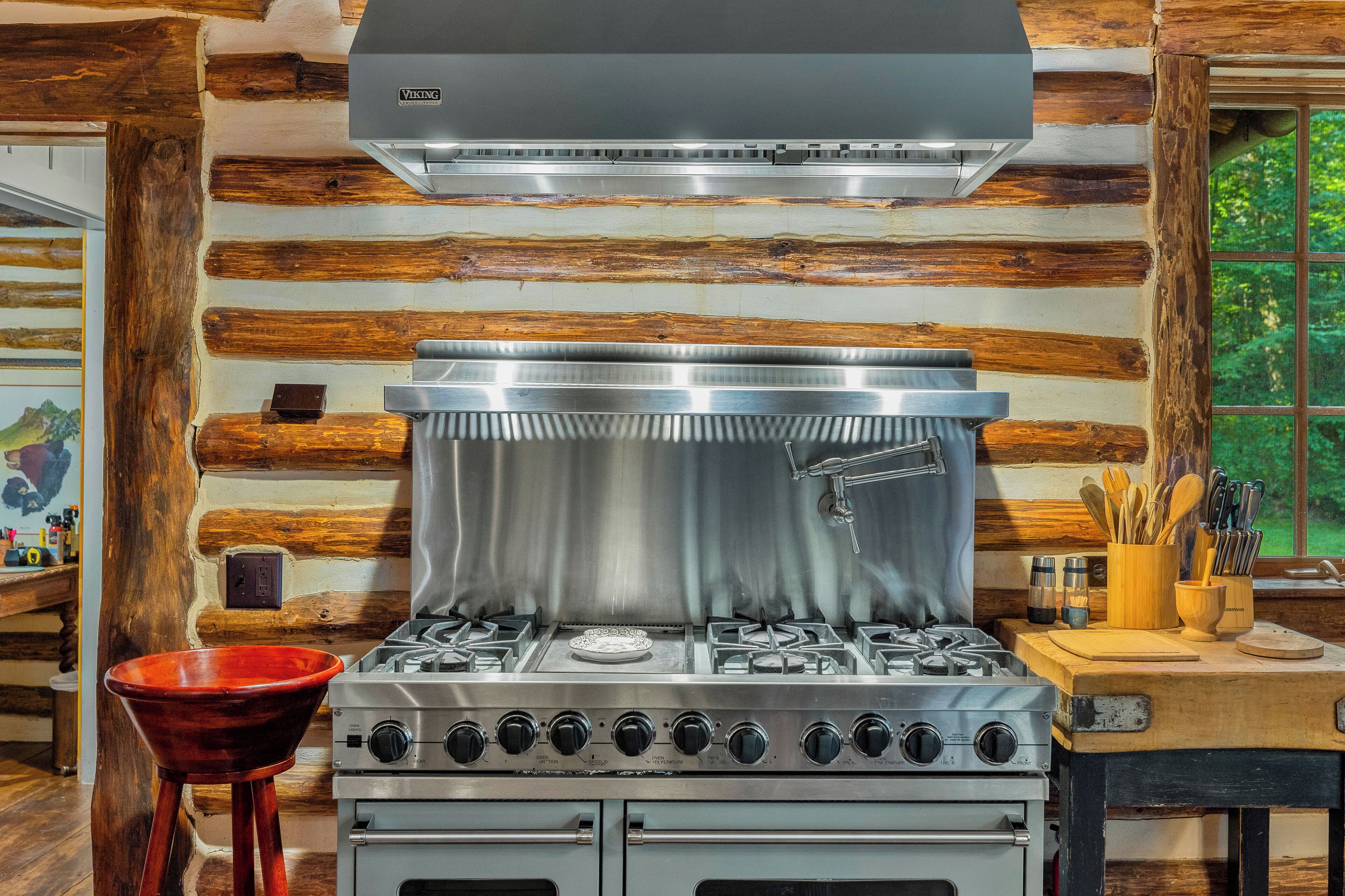Une cuisine dotée d’une cuisinière en acier inoxydable, de murs recouverts de lambris en bois et d’une fenêtre donnant sur un paysage verdoyant.