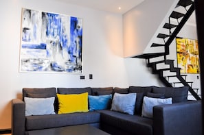 Ein modernes Wohnzimmer mit einem grauen Ecksofa, einem großen abstrakten Gemälde und einer schwarzen Wendeltreppe.