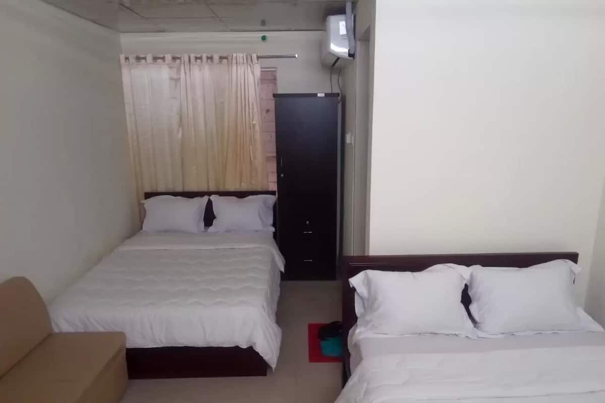 A hotel room with two beds, a sofa, a door, and an air conditioning unit.