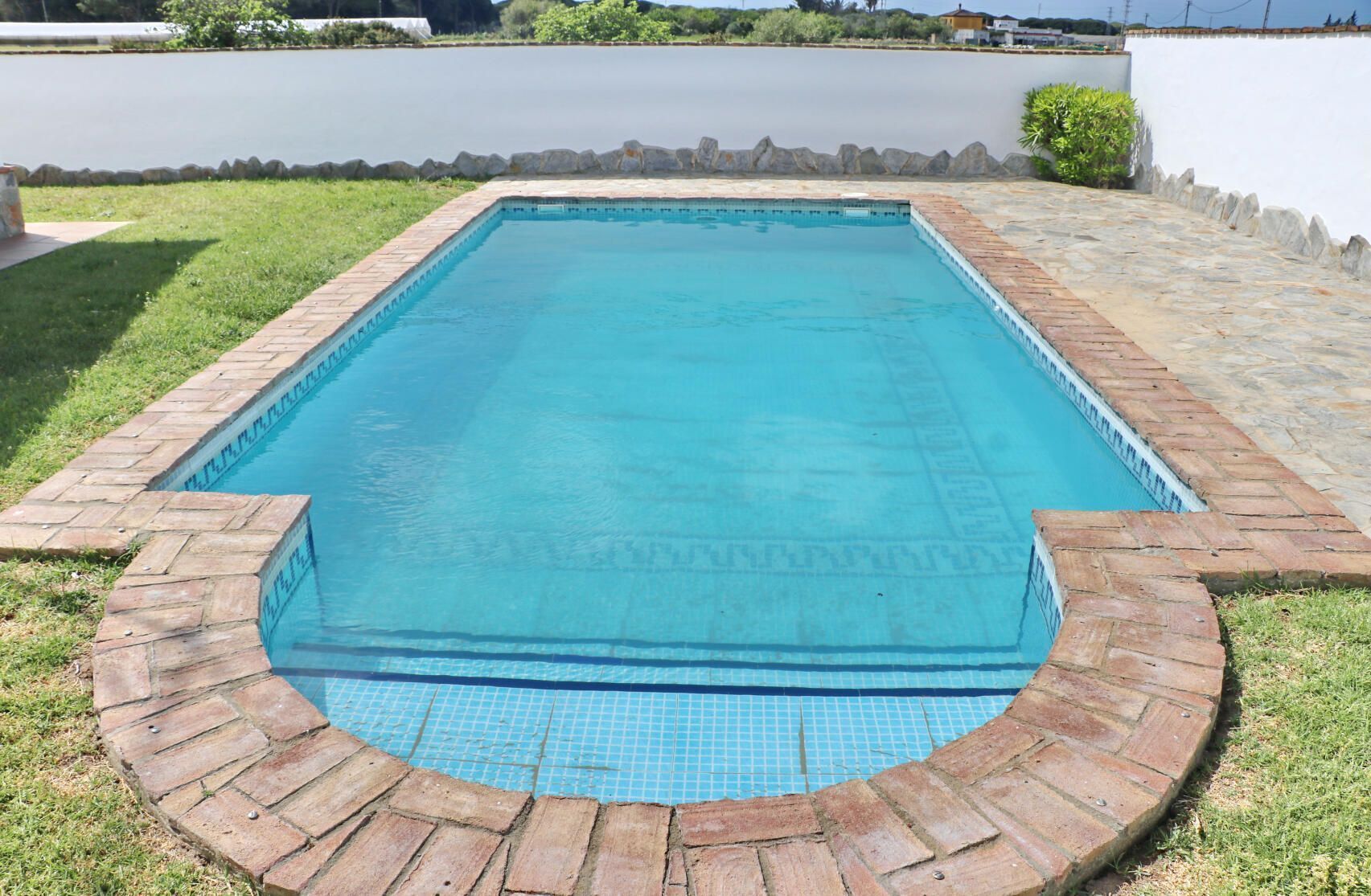 Une piscine rectangulaire avec un bord carrelé et une bordure en briques.