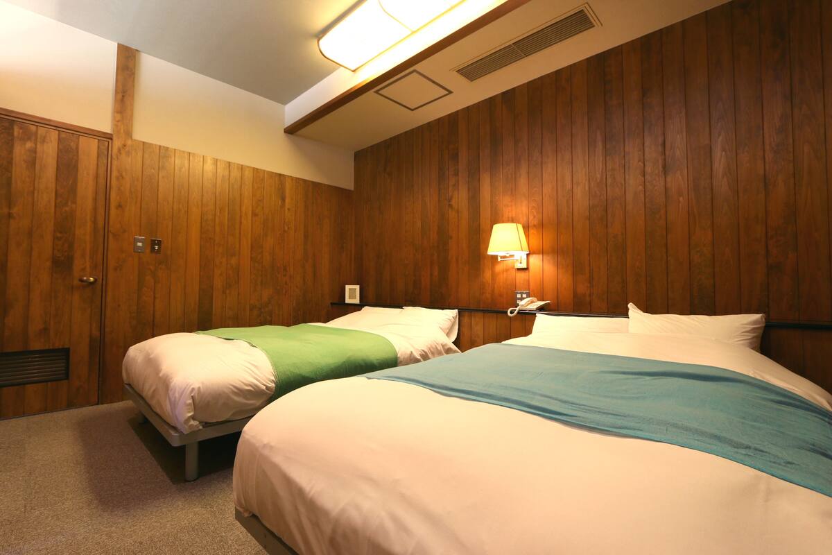 A hotel room with two beds, wooden paneling on the walls, a wall-mounted lamp, and a telephone.