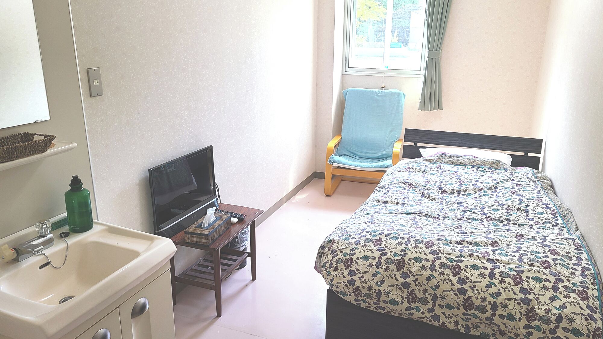 A bedroom with a bed, a chair, a TV, and a sink.