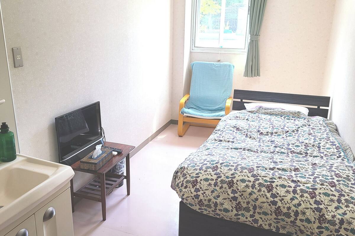 A bedroom with a bed, a chair, a TV, and a sink.