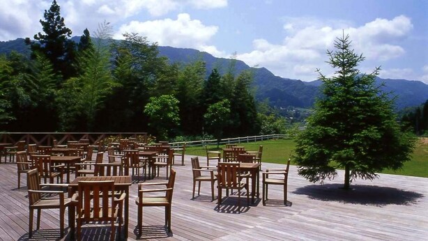 An outdoor seating area with wooden tables and chairs, surrounded by trees and mountains in the background. - Sora no Mori Hotel Hanagori (Kami)