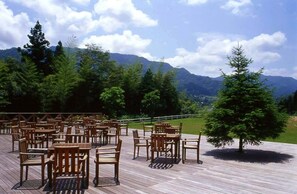 An outdoor seating area with wooden tables and chairs, surrounded by trees and mountains in the background. - Sora no Mori Hotel Hanagori (Kami)