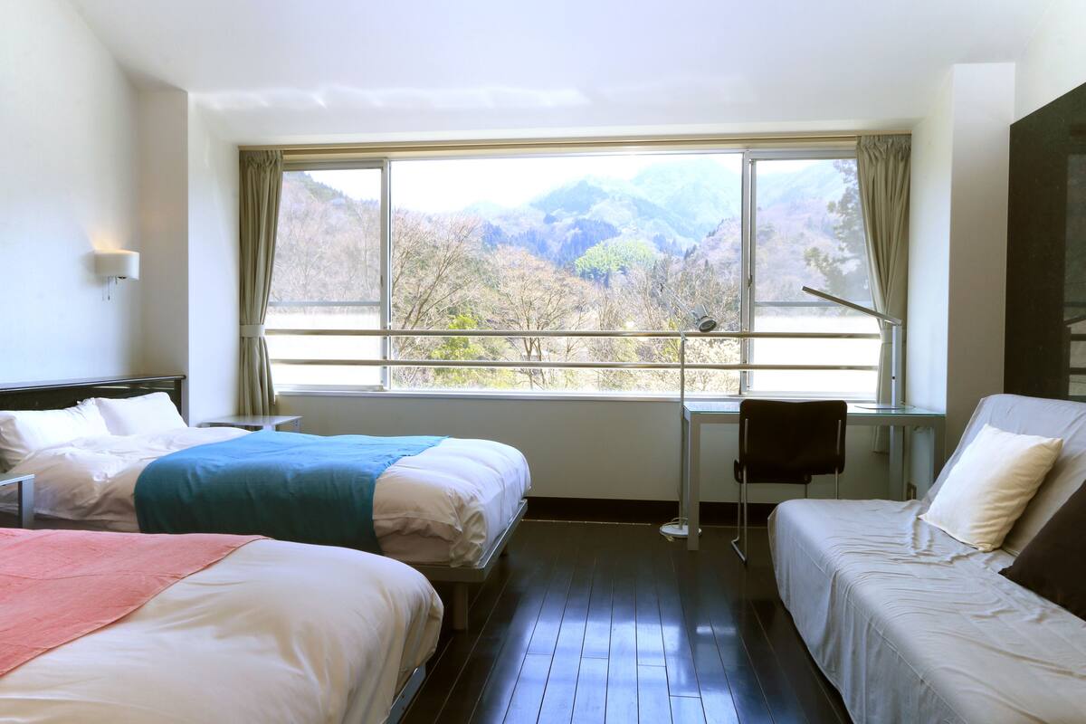 A hotel room with two beds, a desk, and a large window offering a mountain view.