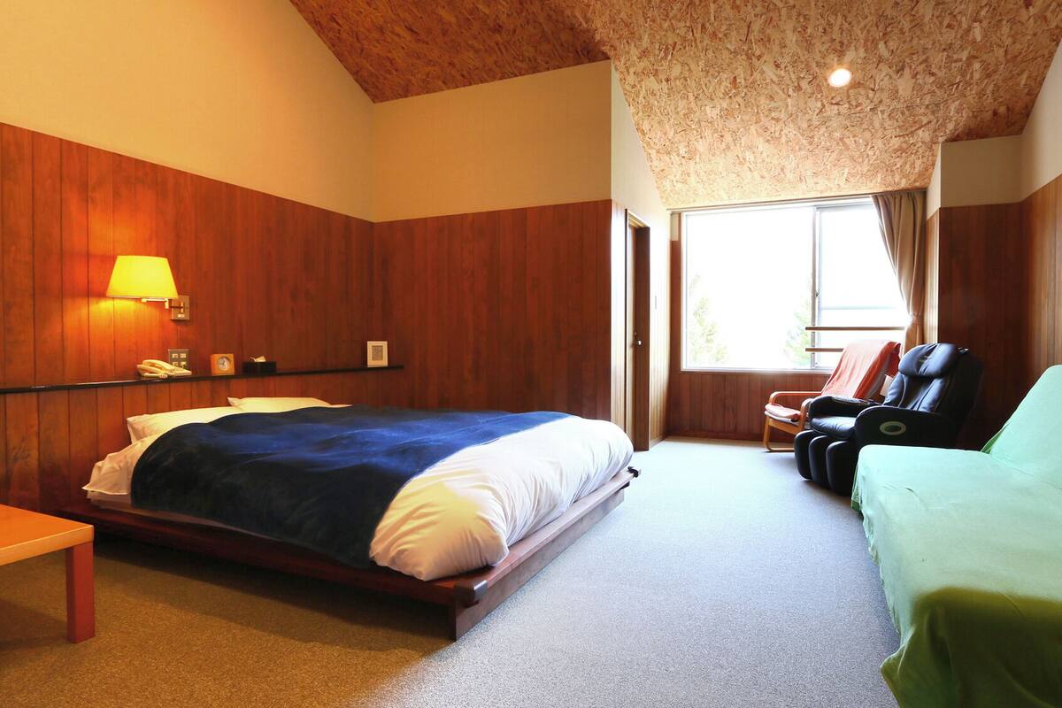 A bedroom with a bed, a massage chair, a bench, and a window.