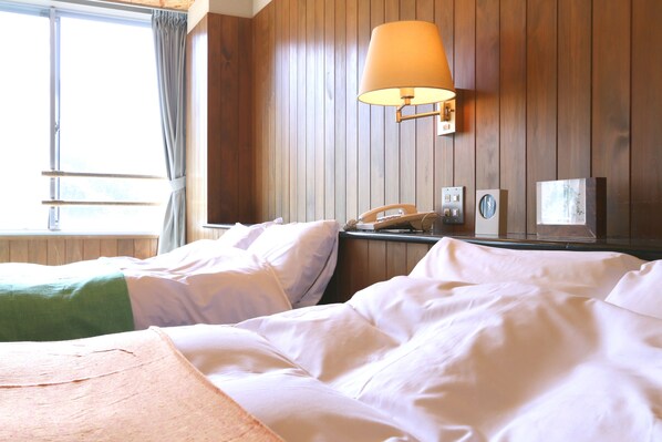 A hotel room with two beds, a lamp, a phone, and a window with curtains.