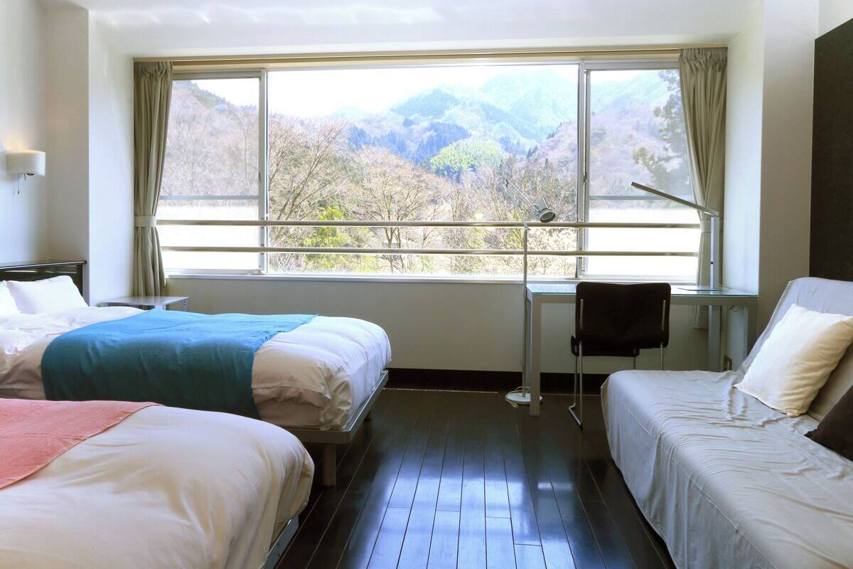 A hotel room with two beds, a desk, and a large window with a mountain view.