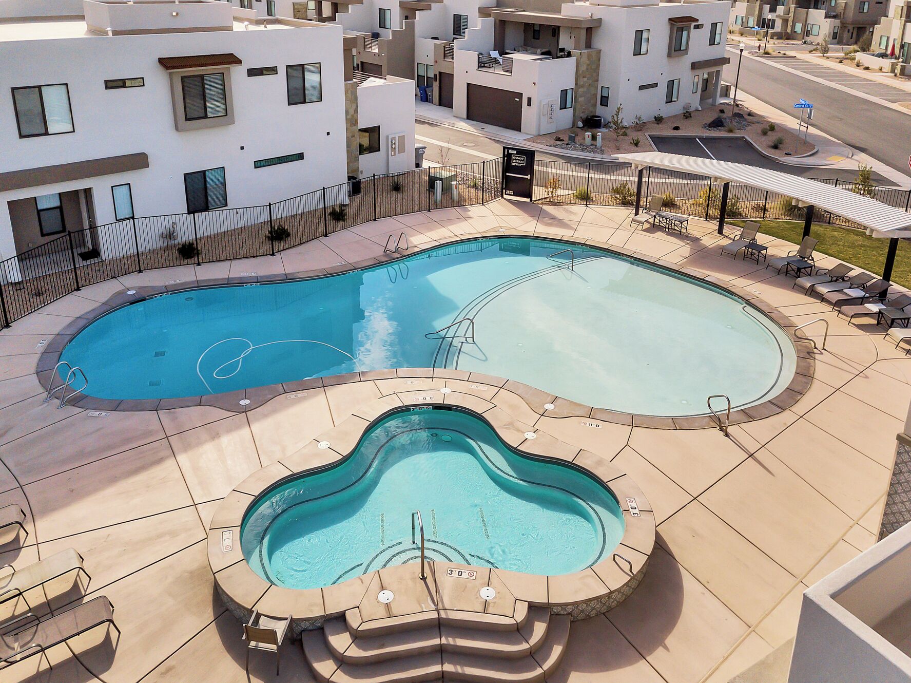 A modern residential complex with a swimming pool area, including a hot tub and lounge chairs.