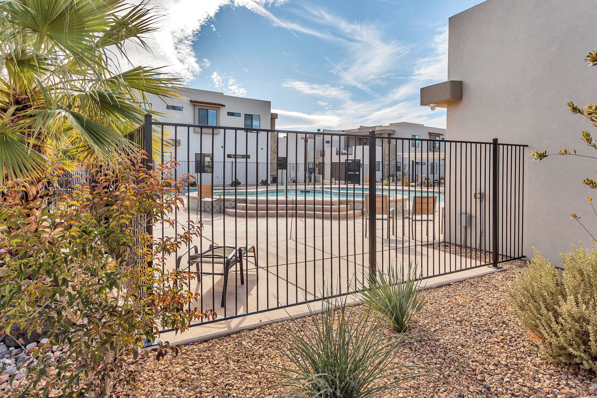 A gated outdoor area with a pool, surrounded by palm trees and a white building.