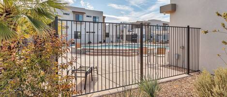 A gated outdoor area with a pool, surrounded by palm trees and a white building.