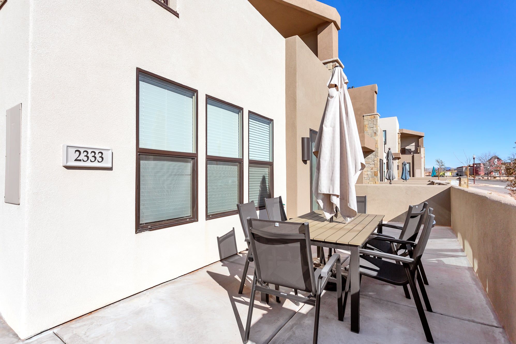 An outdoor patio with a table and chairs, a number sign, and a view of a building in the background.
