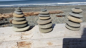 Drie stapels steen op een houten ondergrond aan het strand, met de oceaan op de achtergrond.