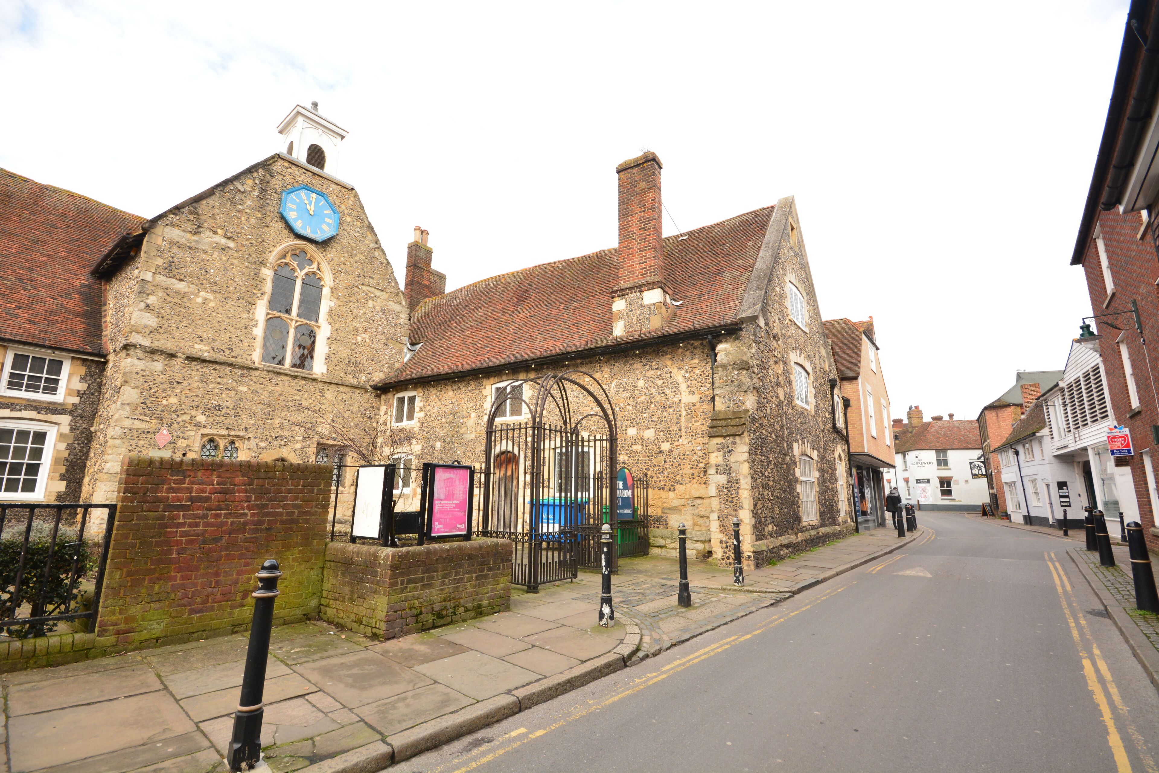 A historic building with a clock tower, a gated entrance, and a street in front.
