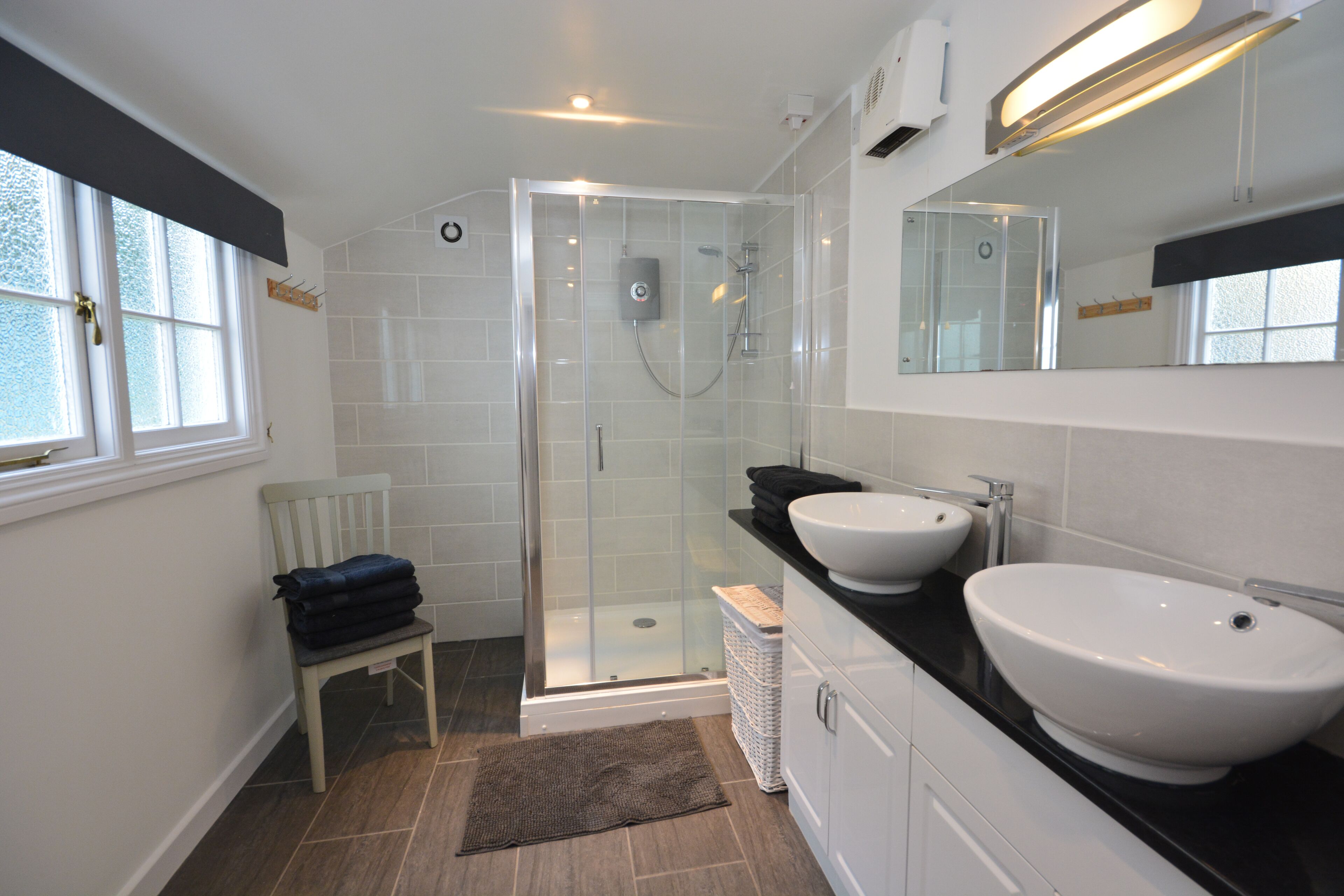 A modern bathroom with a glass-enclosed shower, two sinks, and a mirror above the countertop.