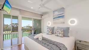 Ein Schlafzimmer mit einem großen Bett, einem Deckenventilator und Blick ins Freie durch eine Schiebetür.
