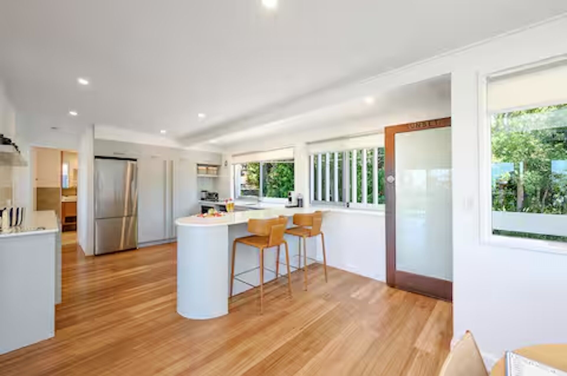 A modern kitchen with a central island, wooden flooring, and a view of the outdoors.