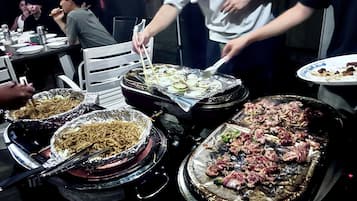 A dining table with various dishes, including noodles, grilled meat, and vegetables.