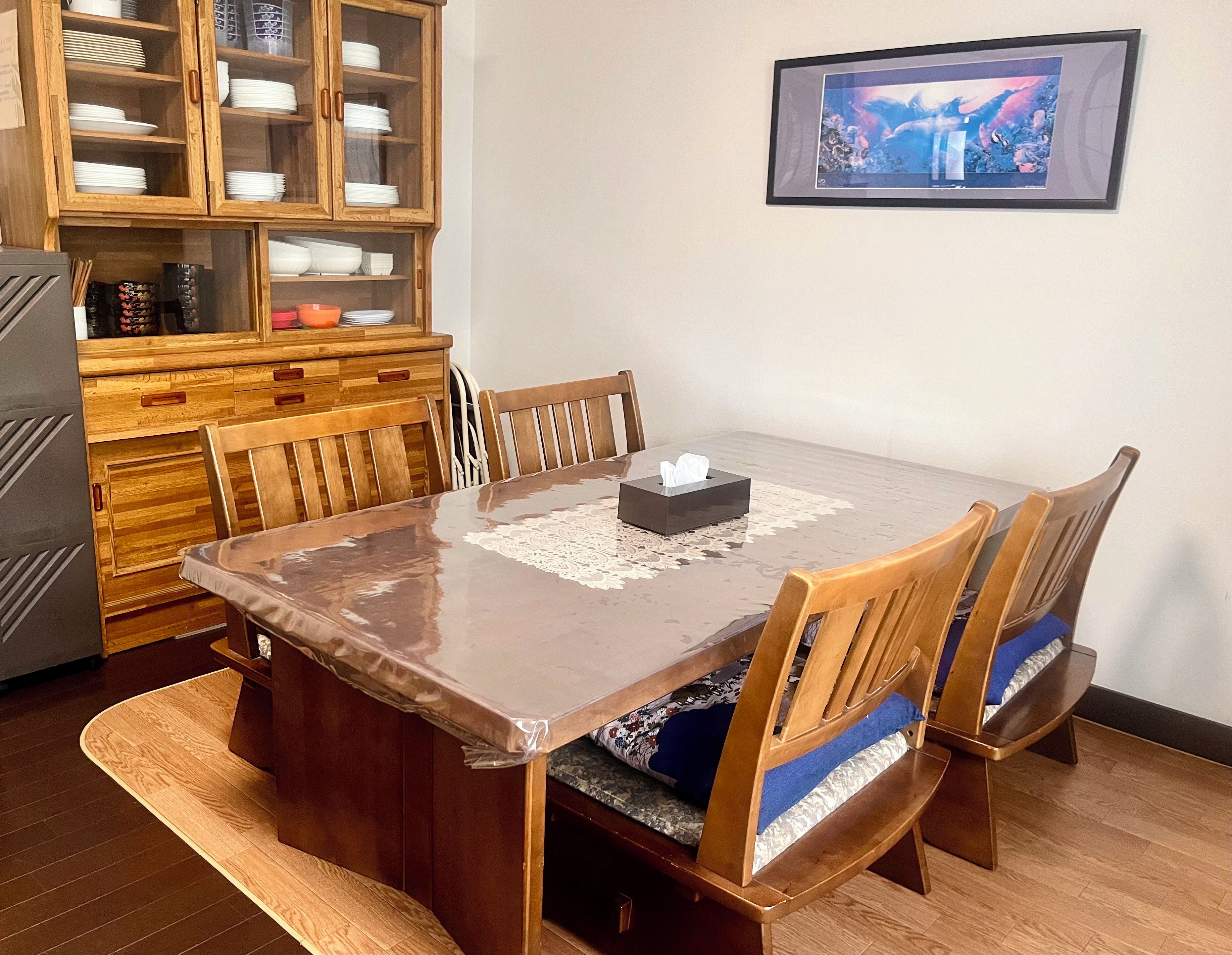 A dining area with a wooden table, chairs, a cabinet with dishes, and a framed picture on the wall.