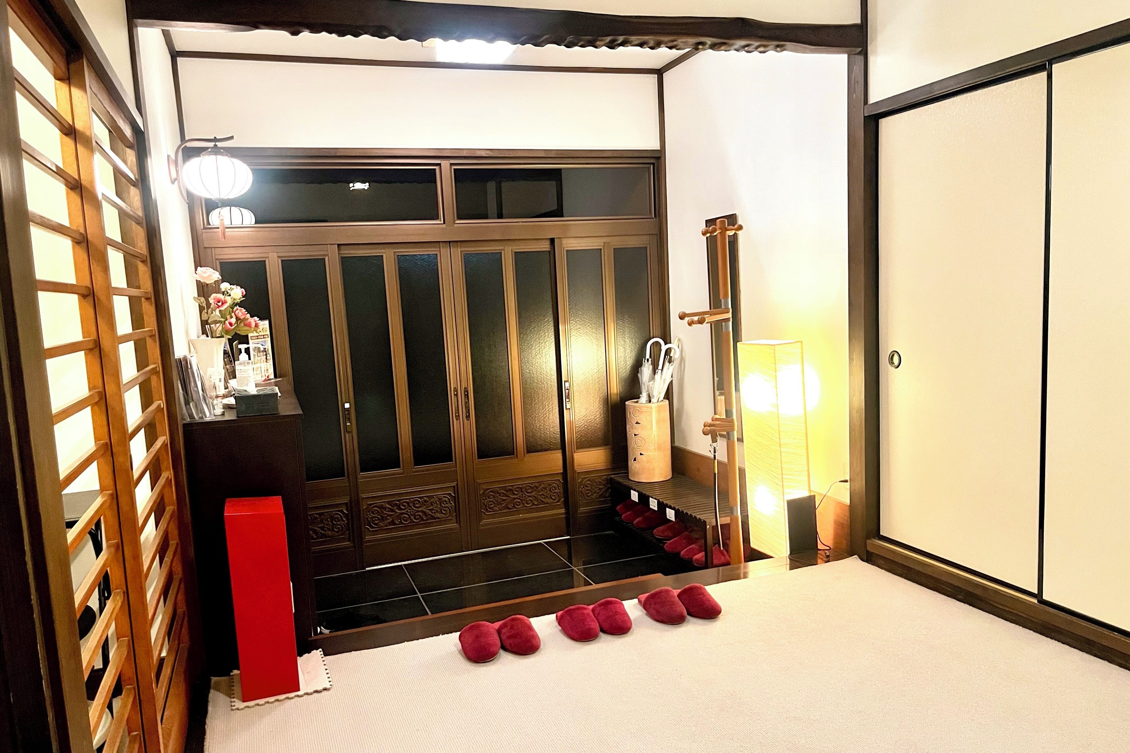 A traditional Japanese room with sliding doors, a wooden desk, a red box, and a row of red slippers.