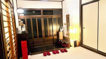 A traditional Japanese room with sliding doors, a wooden desk, a red box, and a row of red slippers.