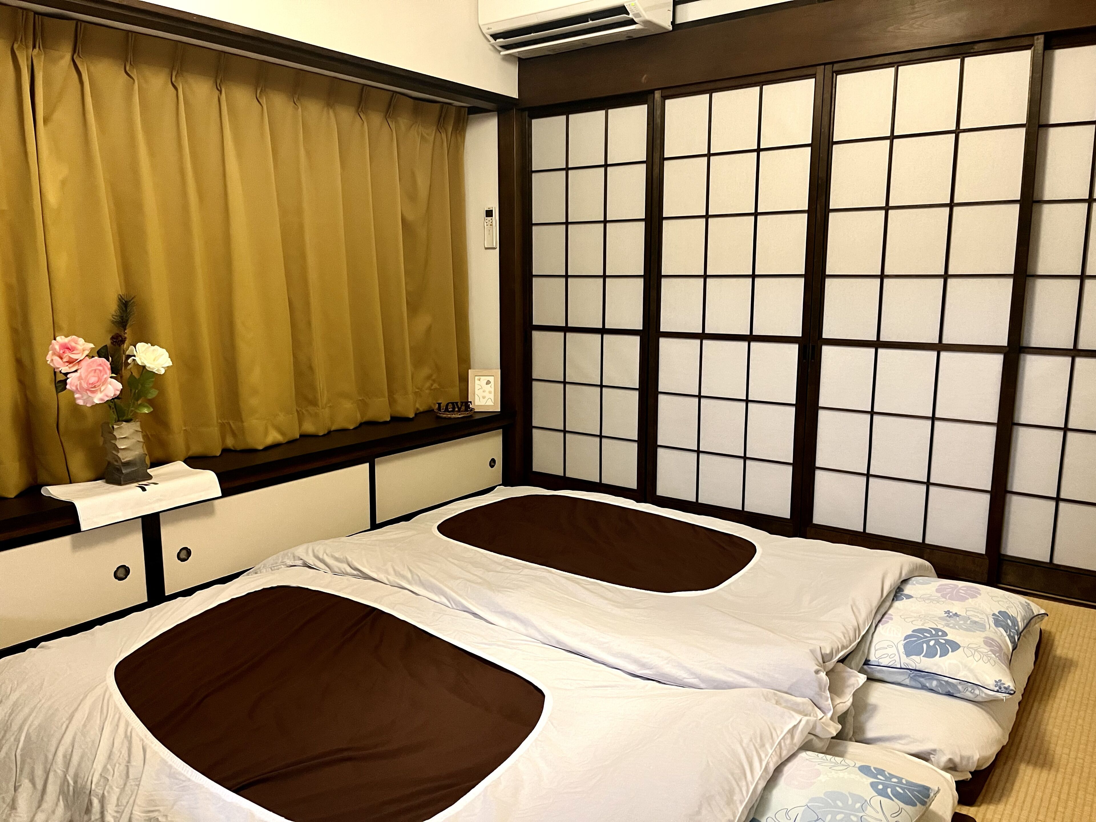 Una habitación tradicional japonesa con suelo de tatami, un panel shoji y una cama con dos almohadas.