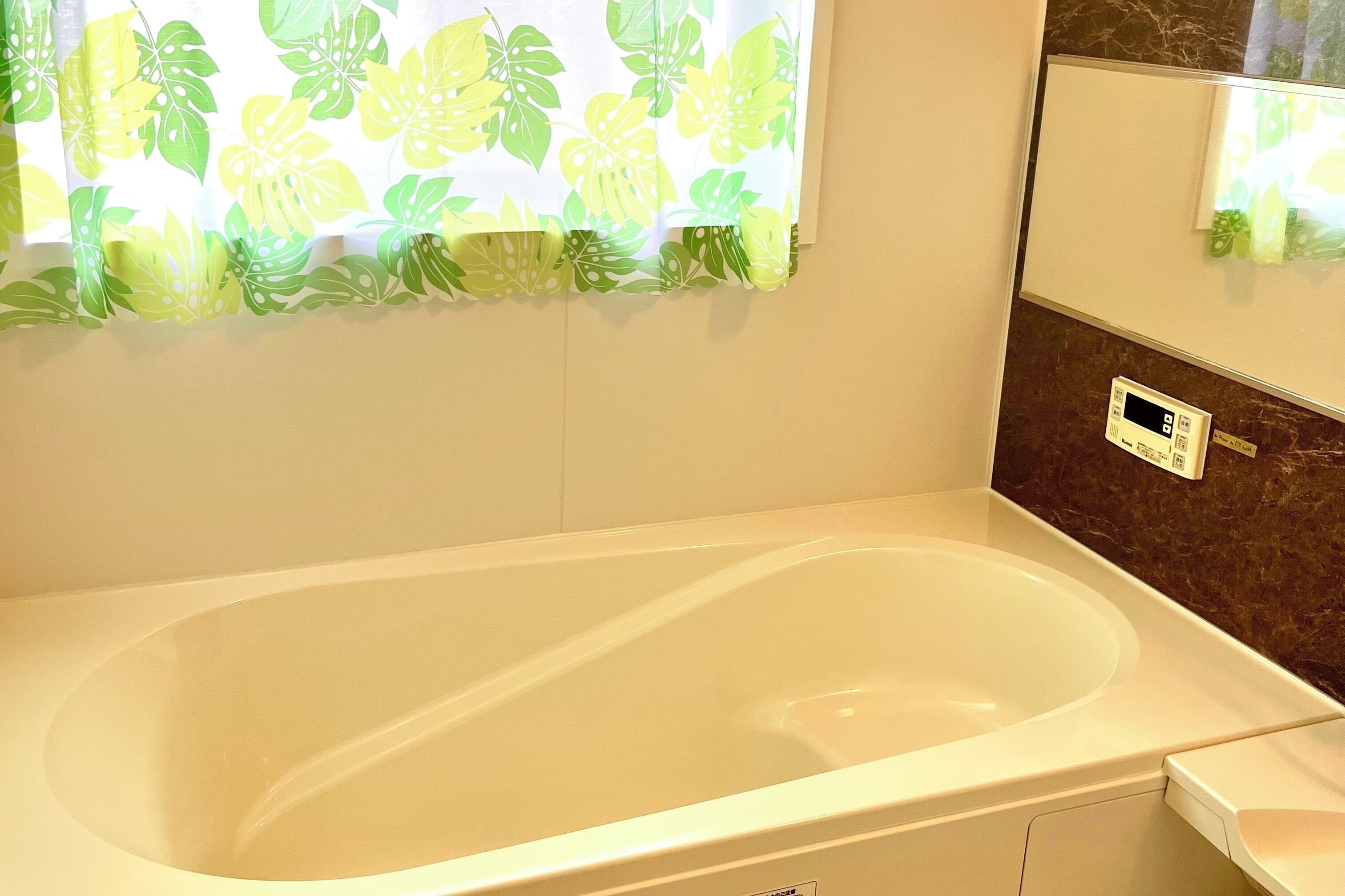 Ein Badezimmer mit Badewanne, Duschbereich, Spiegel und einem an der Wand befestigten Thermostat.