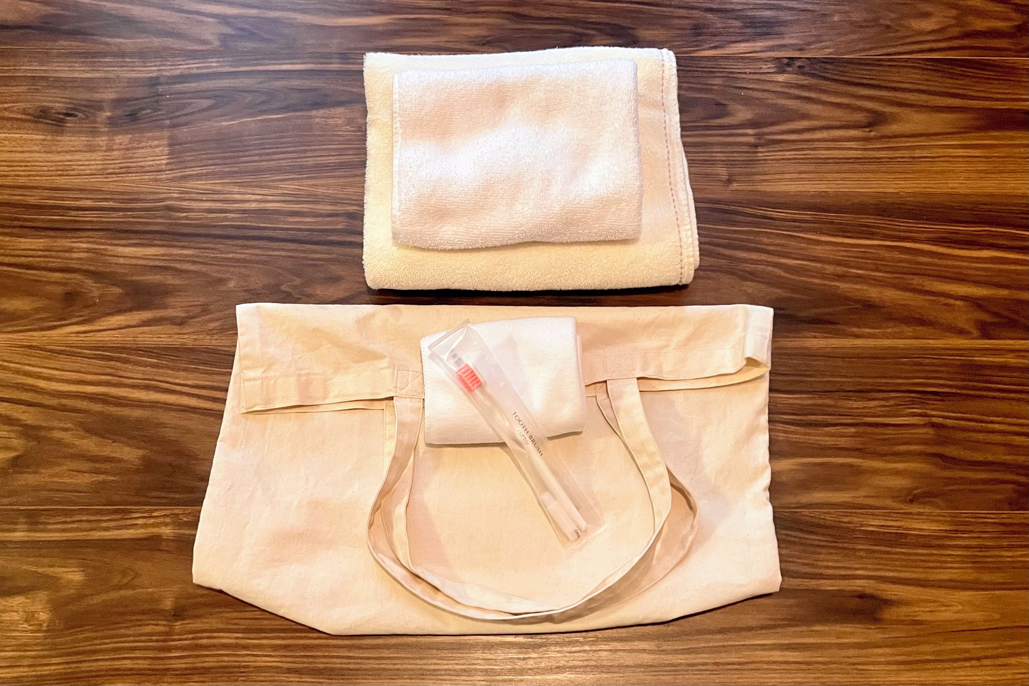Een beige tas met een handgreep en een kleiner beige zakje op een houten oppervlak.