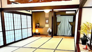 A tatami mat room with a sliding door, a small table with a lamp, and a potted plant. - Mitsuba House (Annaka)