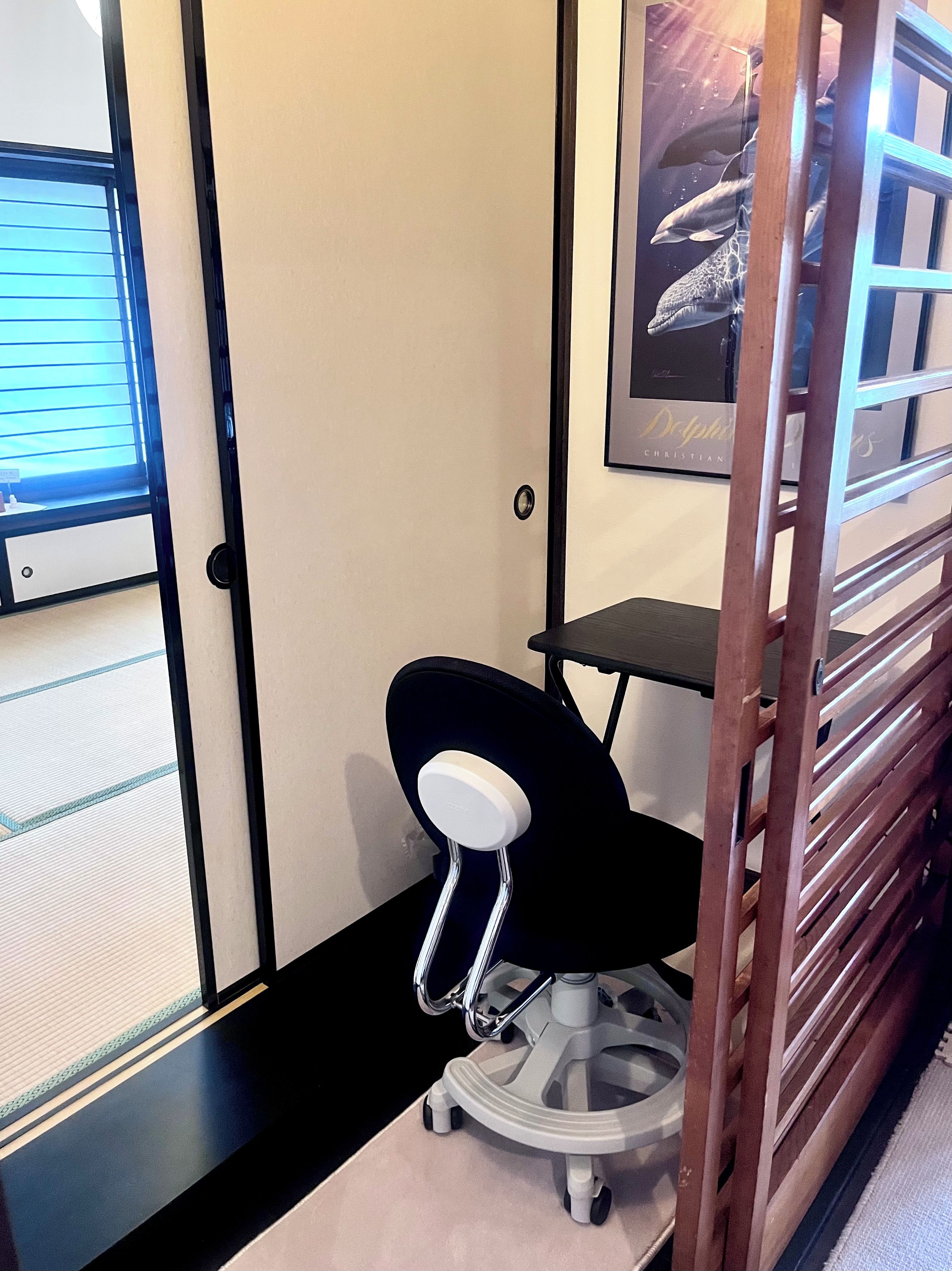 A small, enclosed room with a black chair, a white wall, and a door.