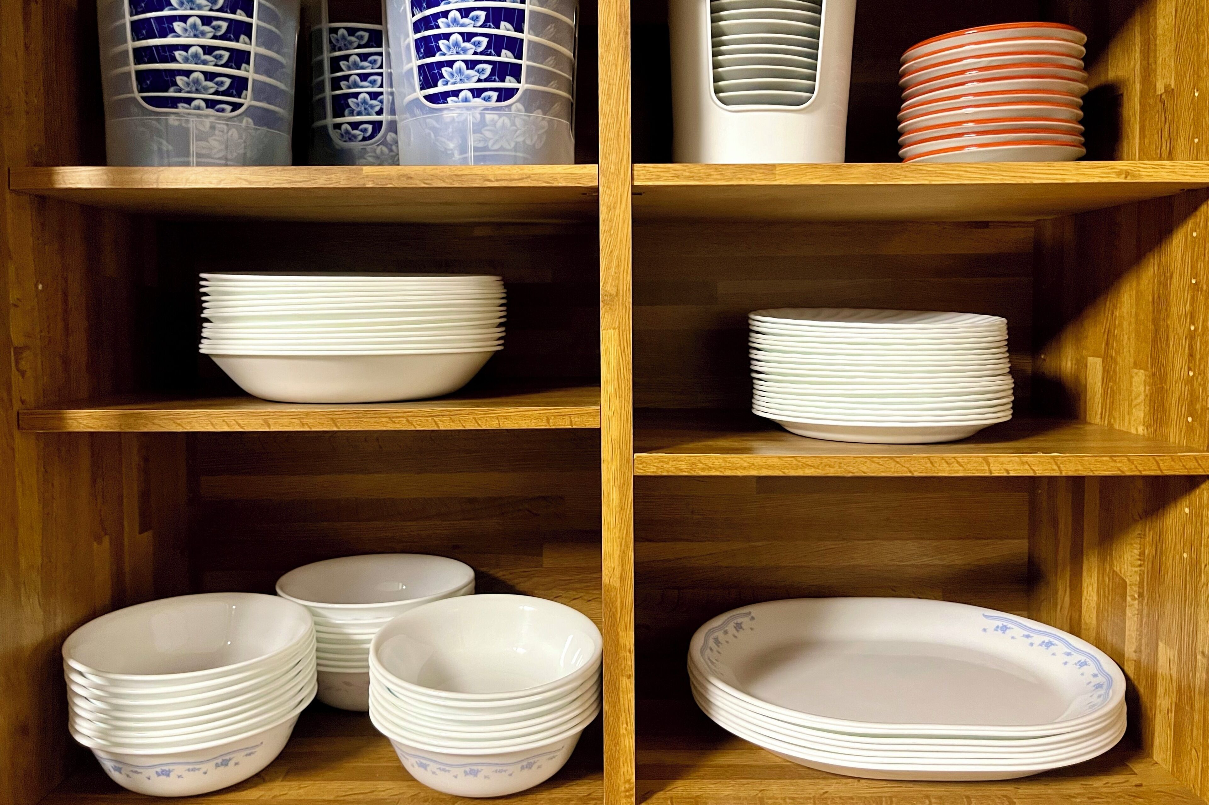 A wooden cabinet with multiple shelves holding stacks of white plates and bowls, some with blue patterns.