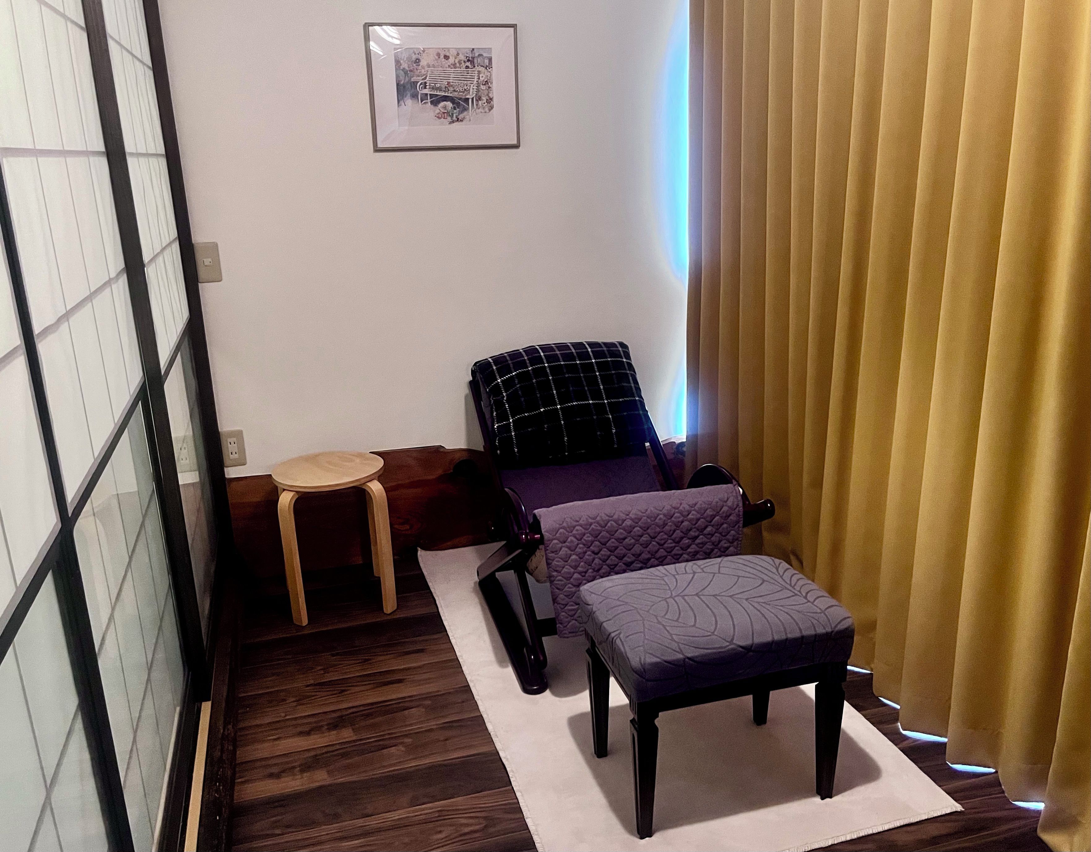 A room with a bed, a chair, a small table, and a window with curtains.