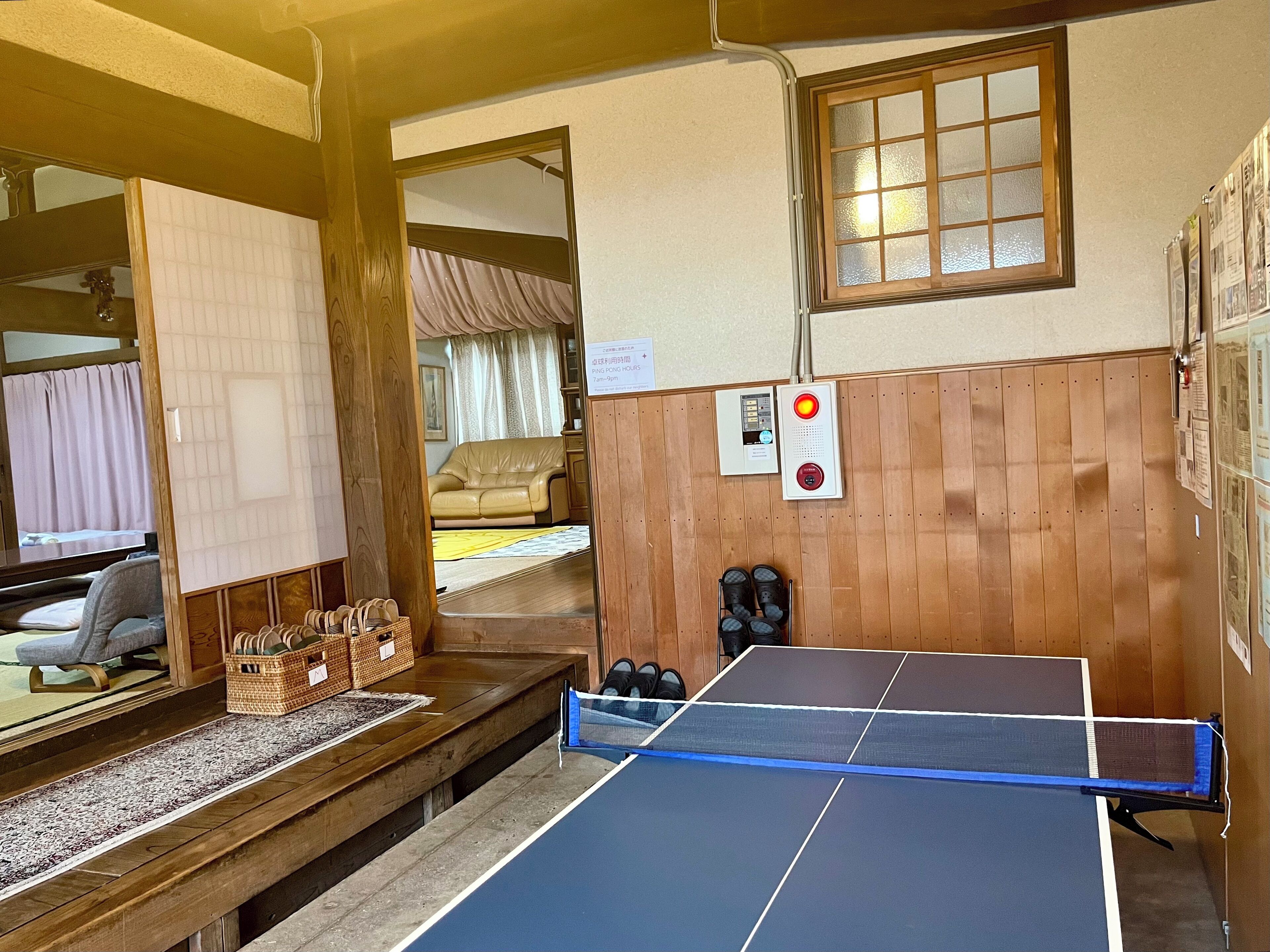 A room with a ping pong table, a wooden bench, a sofa, and a window with blinds.