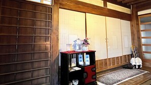 Um quarto japonês tradicional com portas deslizantes, uma pequena vitrine com folhetos e um vaso decorativo com flores.