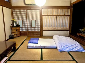 A traditional Japanese room with tatami flooring, a bed with white bedding, a wooden dresser, and a shoji screen.