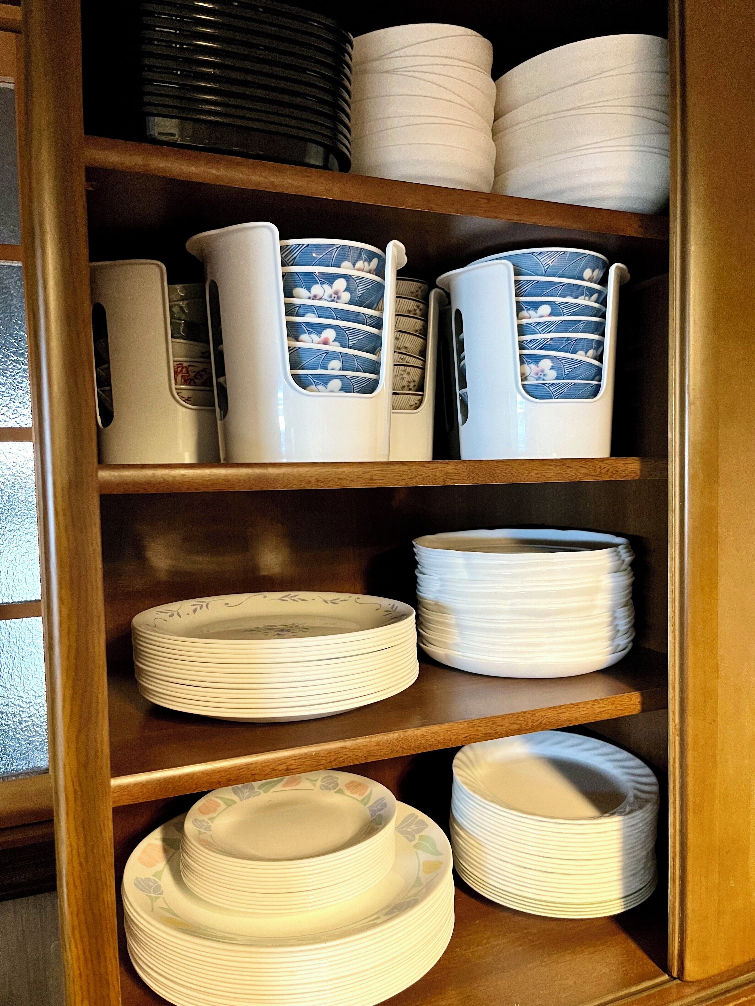 A wooden cabinet with shelves containing white plates, bowls, and a blue and white patterned pitcher.