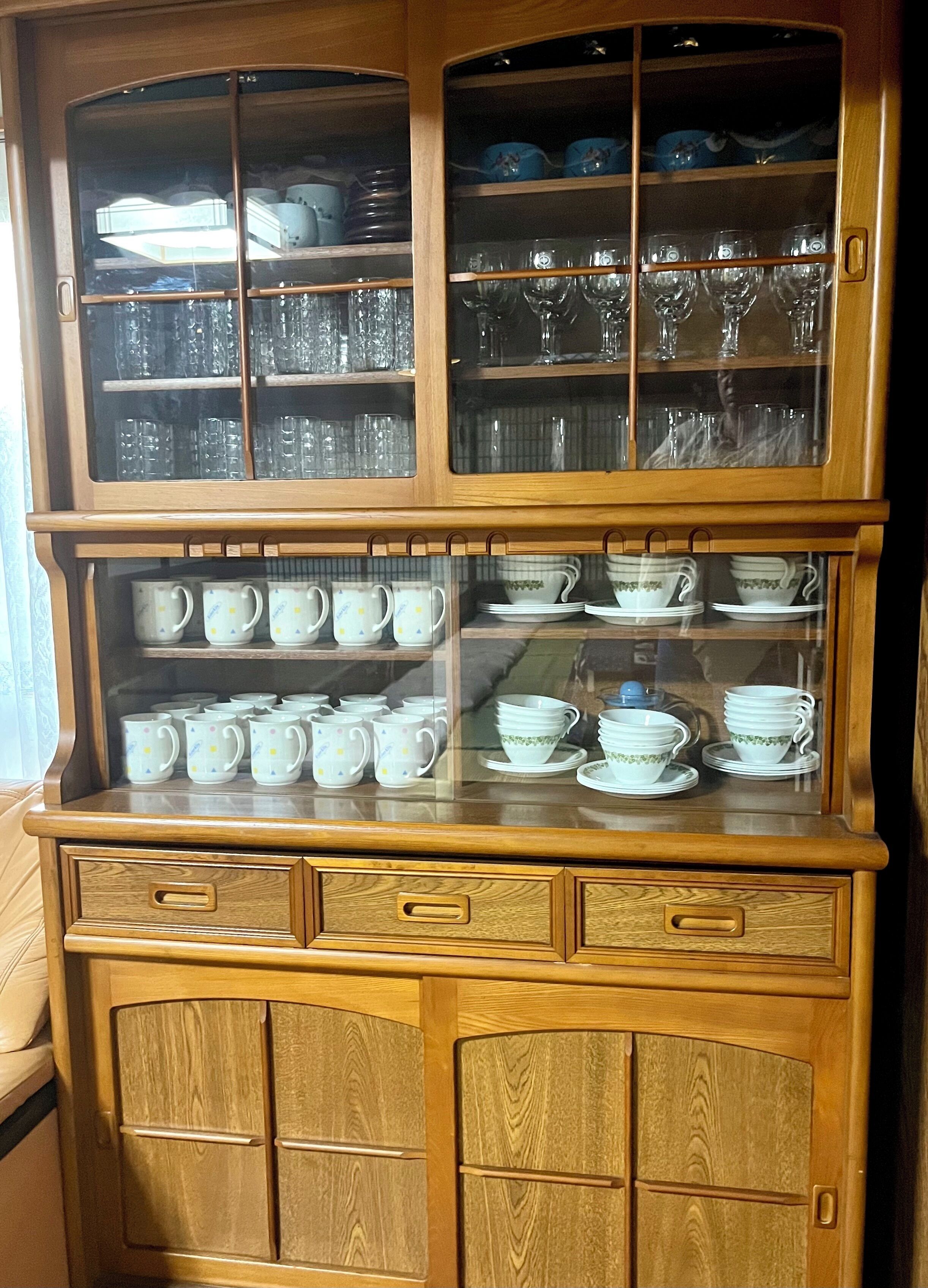 Une vitrine en bois dotée de plusieurs étagères et de tiroirs, contenant divers objets en verre et de la vaisselle en céramique.