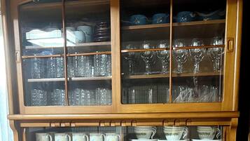 Une vitrine en bois dotée de plusieurs étagères et de tiroirs, contenant divers objets en verre et de la vaisselle en céramique.