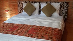 Una cama con una colcha estampada, dos almohadas y un cuadro en una pared de ladrillo.